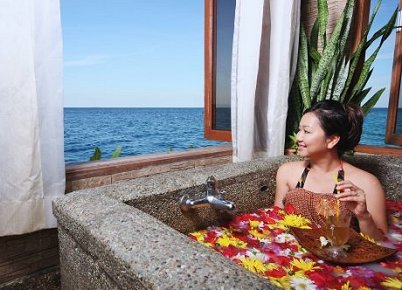 Guest in a flower bath beside a sea-view window at the Ka'andaman Spa