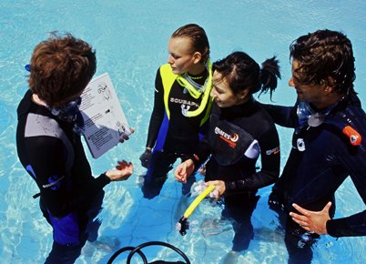Dive instructor briefing three students in shallow water
